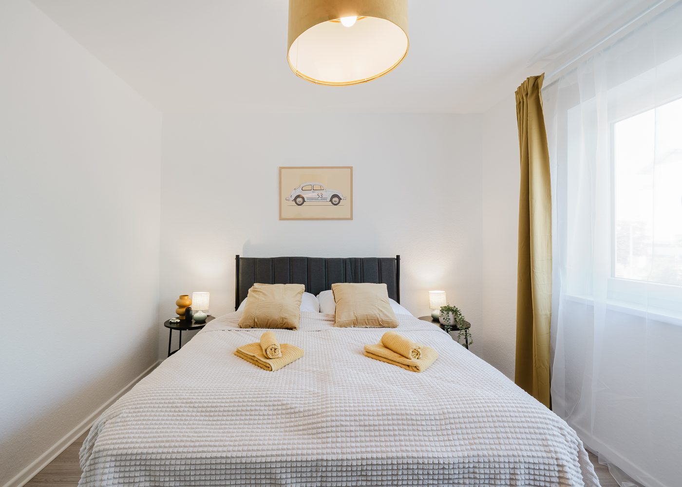 Schlafzimmer des Beetle Apartments in Wolfsburg mit Doppelbett, Nachttischlampen und Käfer-Bild