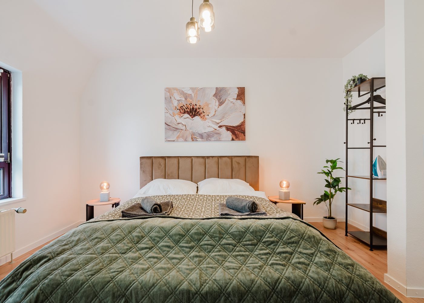 Schlafbereich des Kirchenblick-Lofts mit Doppelbett, grüner Tagesdecke und Kleiderstange